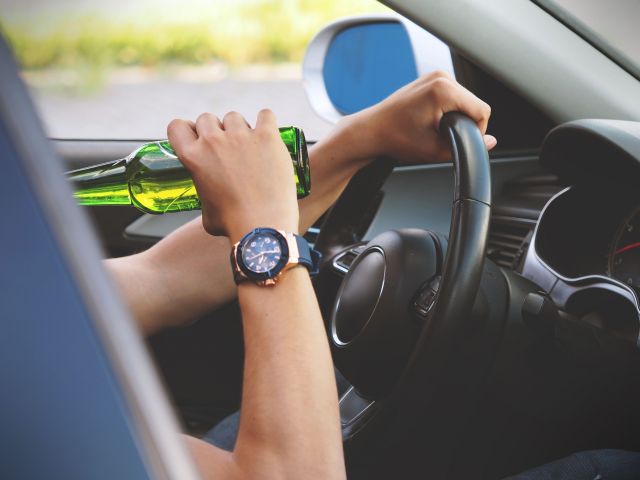 Close up of hand holding beer bottle while driving a car